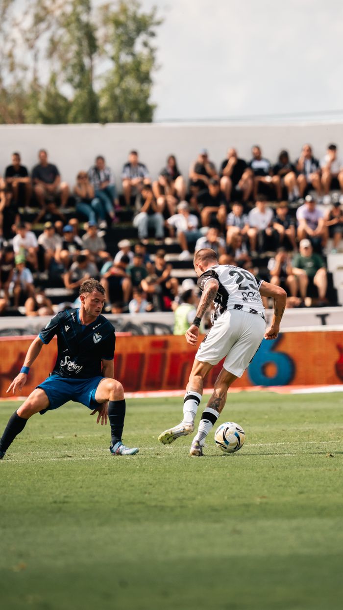Two soccer players in action during a match with a crowd in the stands on a sunny day.